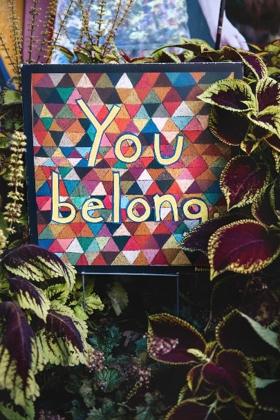 Kukkien keskellä taulu, jossa lukee teksti: You belong.